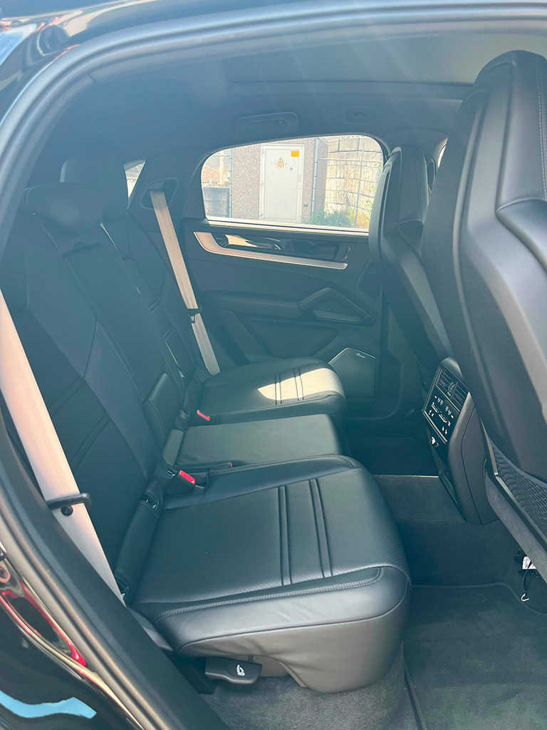 Zicht op de luxe zwart lederen achterbank van een Porsche Cayenne S door een geopende achterdeur