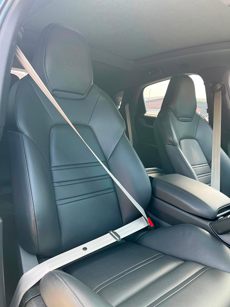 Detailopname van het interieur van een Porsche Cayenne S, tonend de geperforeerde zwart lederen voorstoelen en een contrasterende lichte veiligheidsgordel