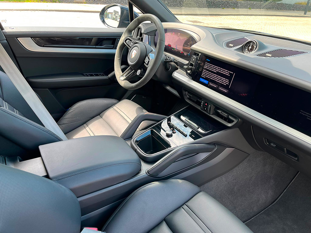 Interieur van een Porsche Cayenne S vanaf de passagierszijde, tonend het infotainmentscherm, de middenconsole en het digitale instrumentenpaneel