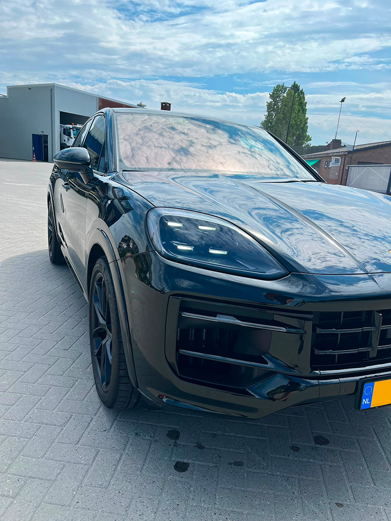 Detailopname van de LED-matrix koplamp en de glanzend zwarte carrosserie van een Porsche Cayenne S op een oprit