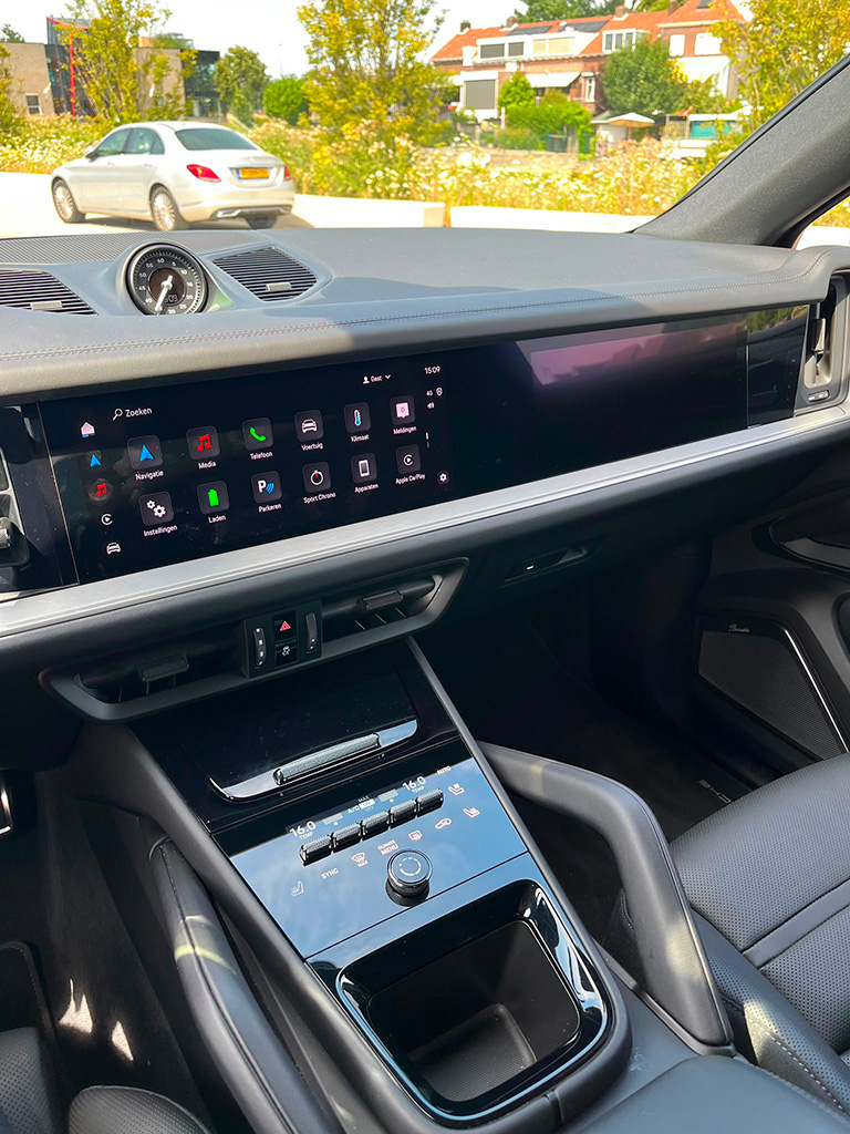 Detailopname van de middenconsole en het dashboard van een Porsche Cayenne S, met het digitale infotainmentscherm en de glanzend zwarte klimaatbediening