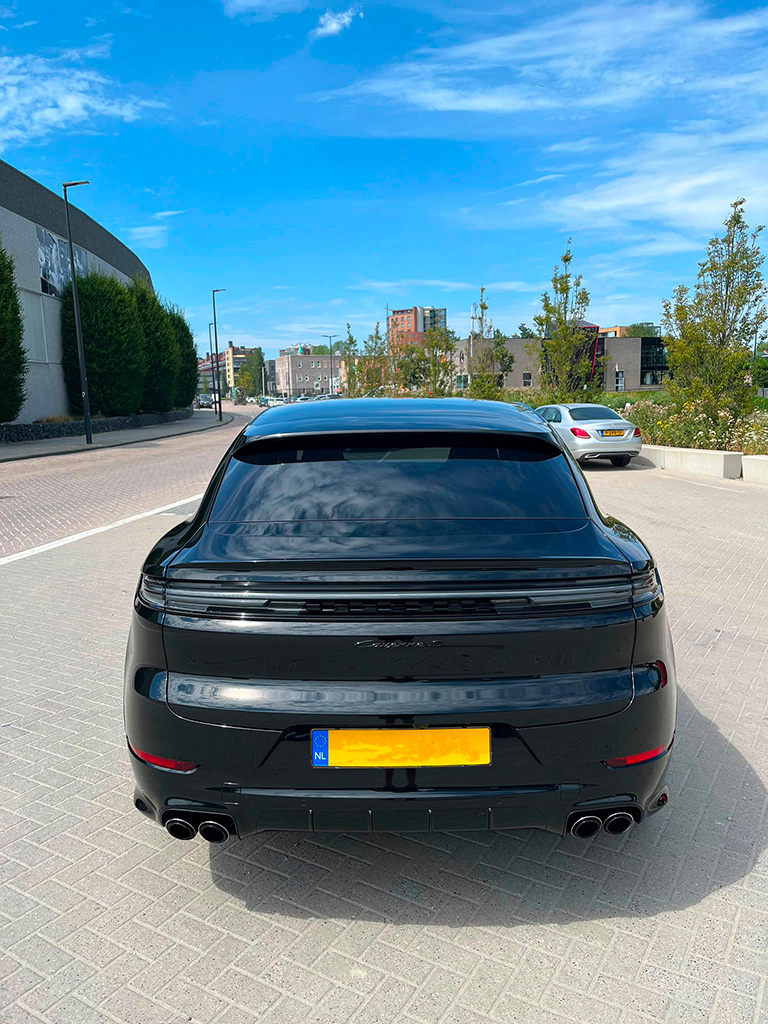 Directe achterzijde van een zwarte Porsche Cayenne S Coupé, tonend de doorlopende achterlichten en achterspoiler onder een blauwe lucht