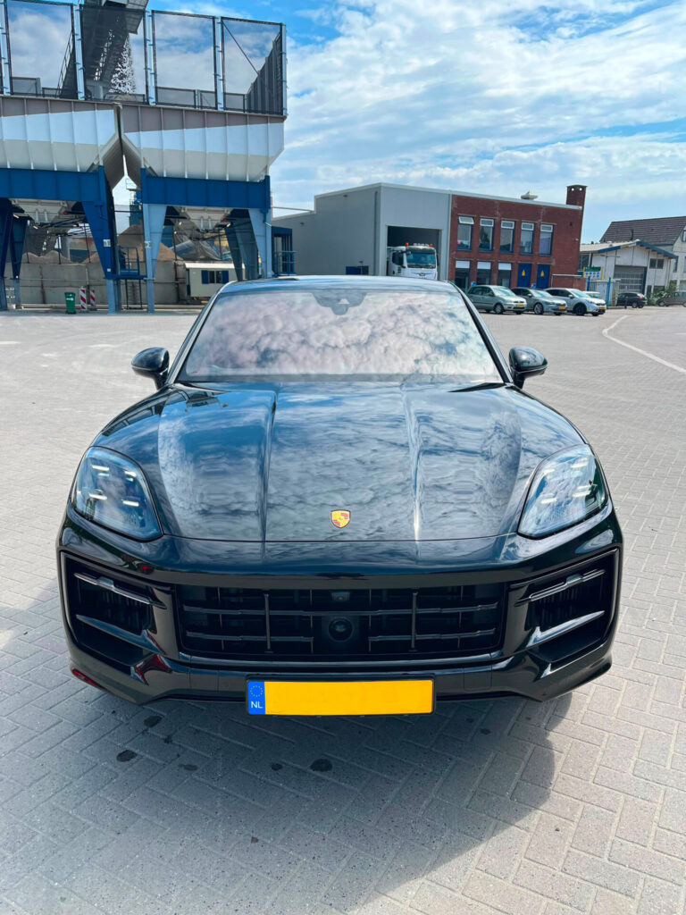Directe voorkant van een zwarte Porsche Cayenne S Coupé, met de wolken weerspiegeld in de motorkap en de voorruit