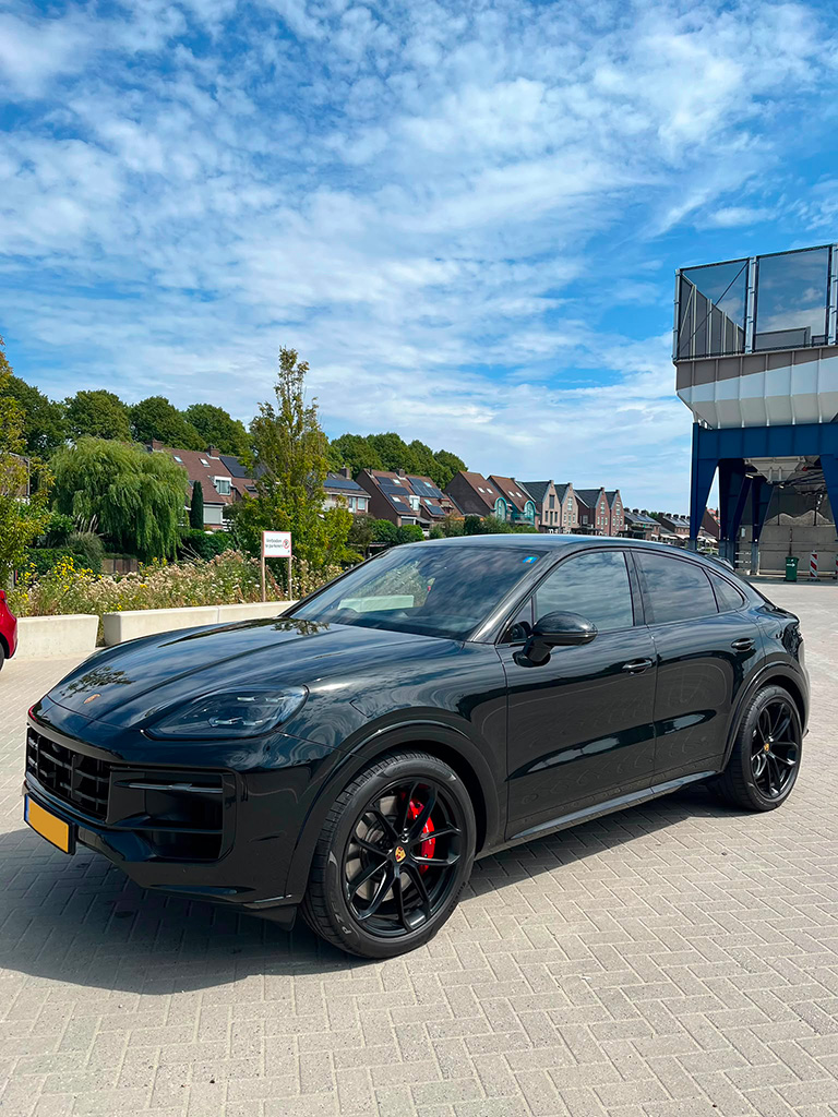 Driekwart zijaanzicht van een glanzend zwarte Porsche Cayenne S Coupé met sportieve zwarte velgen en rode remklauwen